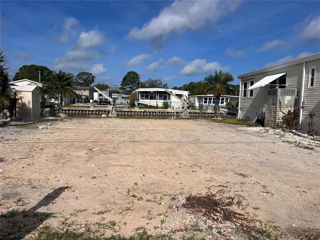 A vacant, sandy waterfront lot features a seawall and boat lift under a blue sky — 105 SCHOONER DRIVE UNIT 105, PALM HARBOR, FL