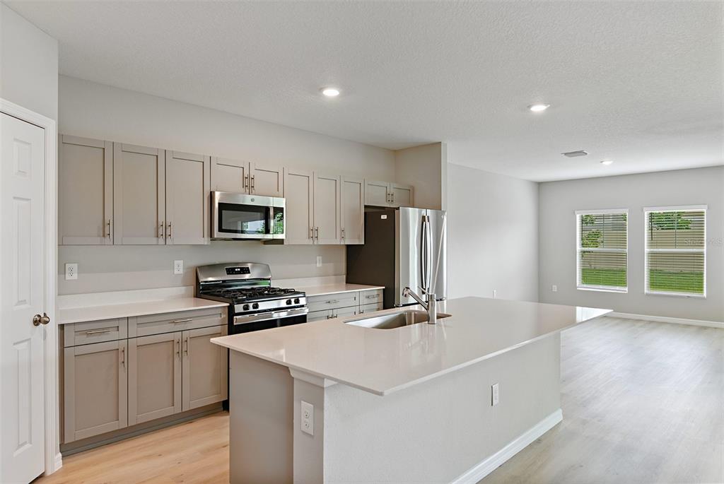 A kitchen features light gray cabinets, stainless steel appliances, and a central quartz island — 4437 RIVERBEND BOULEVARD, HAINES CITY, FL