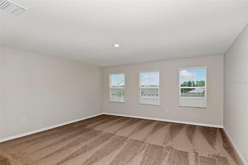 An empty bedroom features beige walls, brown carpet, and three windows with white blinds — 4437 RIVERBEND BOULEVARD, HAINES CITY, FL