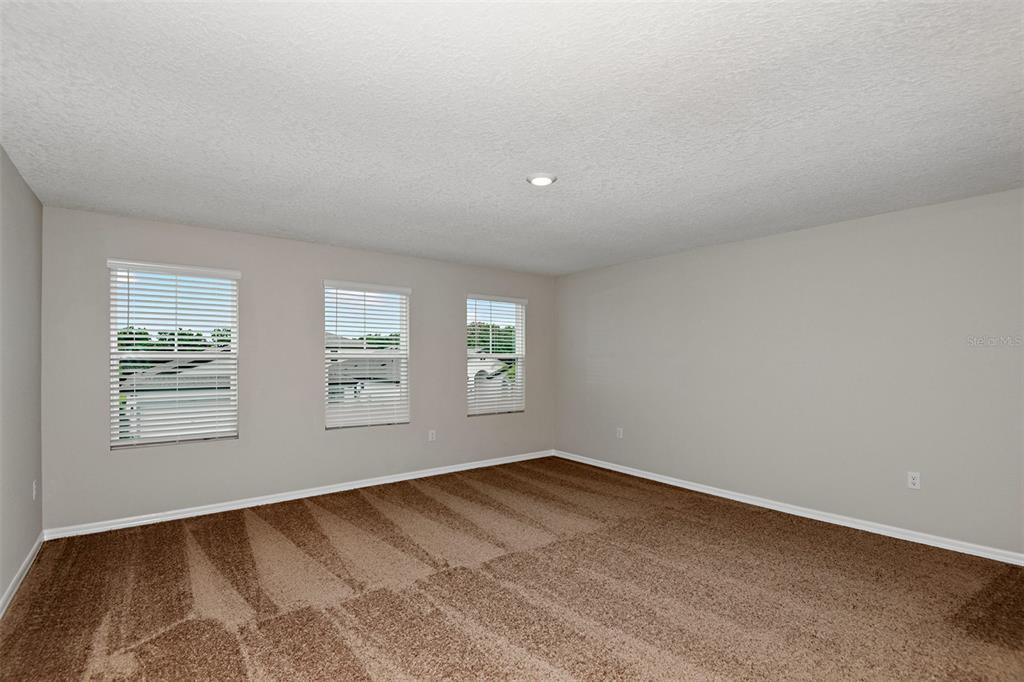 An empty room with beige walls, brown carpet, and three windows with white blinds — 4437 RIVERBEND BOULEVARD, HAINES CITY, FL