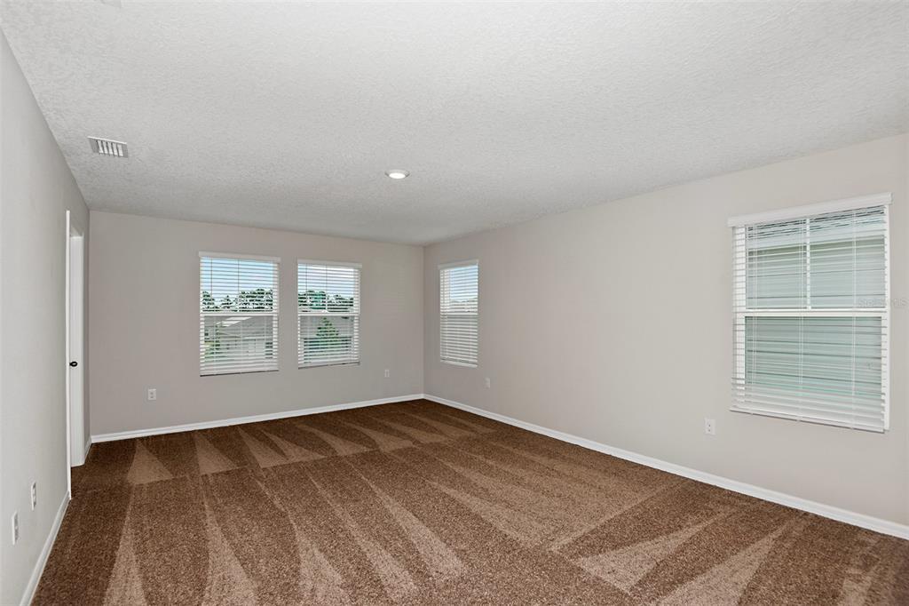 An empty room with beige walls, brown carpet, and several windows with white blinds — 4437 RIVERBEND BOULEVARD, HAINES CITY, FL