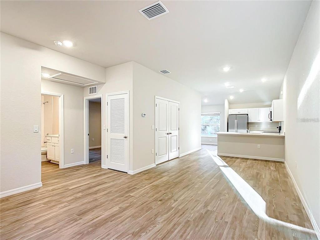 An open-concept living area features light wood-look flooring, white walls, and an adjacent kitchen — 3070 E ODIER STREET, INVERNESS, FL