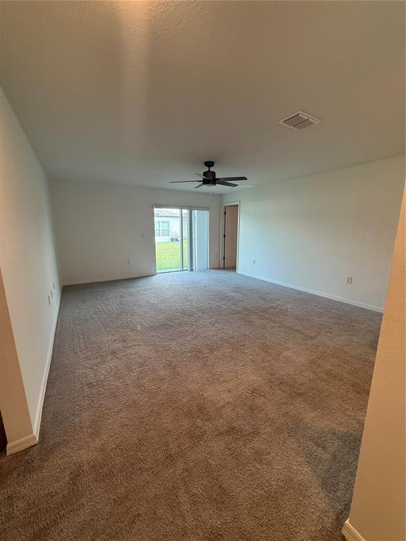A large, carpeted room features a ceiling fan, white walls, and a sliding glass door — 46 WILLOW LANE, POINCIANA, FL