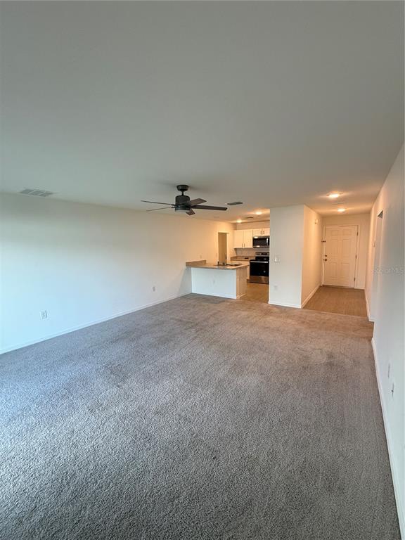An open-concept living area with gray carpeting, a ceiling fan, and an adjacent kitchen — 46 WILLOW LANE, POINCIANA, FL
