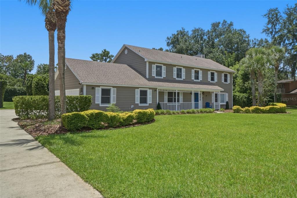 A two-story house with tan siding, white shutters, and a front porch sits on a lawn — 2143 BLUE IRIS PLACE, LONGWOOD, FL