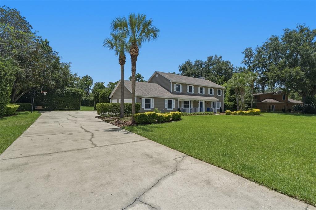 A two-story house with a large concrete driveway, palm trees, and a green lawn — 2143 BLUE IRIS PLACE, LONGWOOD, FL