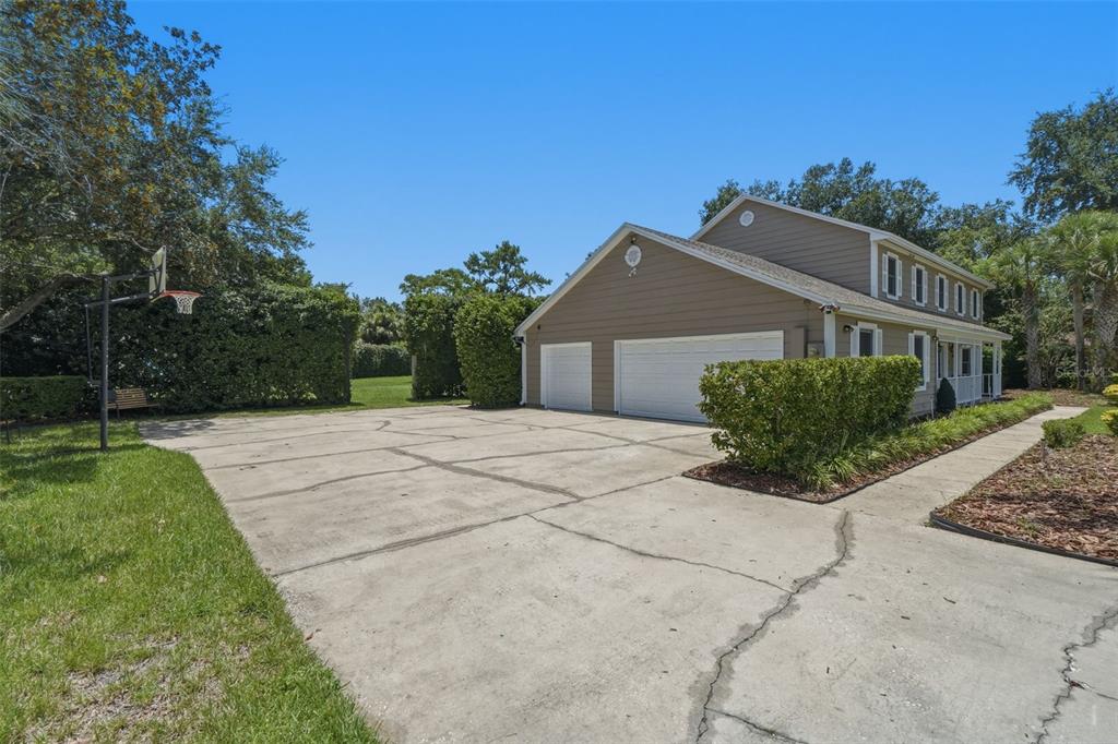 A tan house with a multi-car garage and a large cracked concrete driveway — 2143 BLUE IRIS PLACE, LONGWOOD, FL