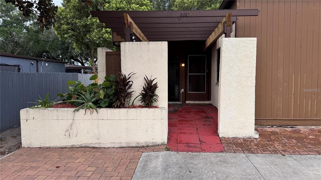 A stucco-walled entryway features a wooden pergola, a red-tiled walkway, and a raised planter bed — 2657 EXUMA WAY, WINTER PARK, FL