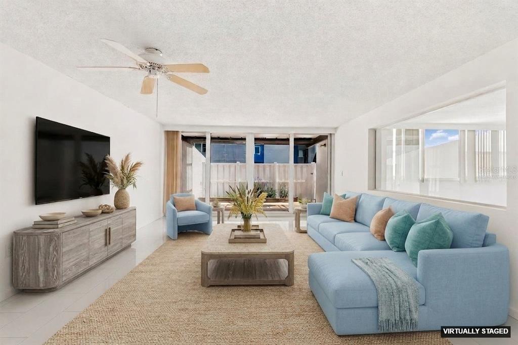 A bright, empty living room features white tile floors, a ceiling fan, and sliding glass doors — 450 TREASURE ISLAND CAUSEWAY UNIT 106, TREASURE ISLAND, FL