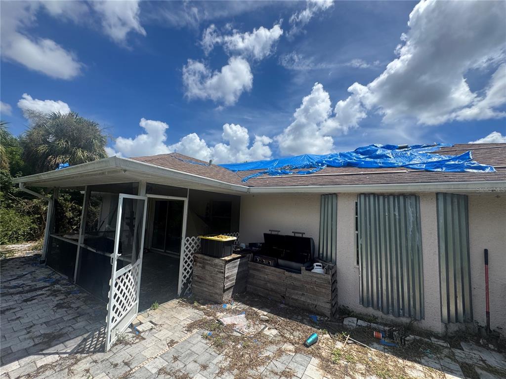The exterior of a house features a screened-in patio and a blue tarp on the roof — 168 MILLPORT STREET NW, PORT CHARLOTTE, FL