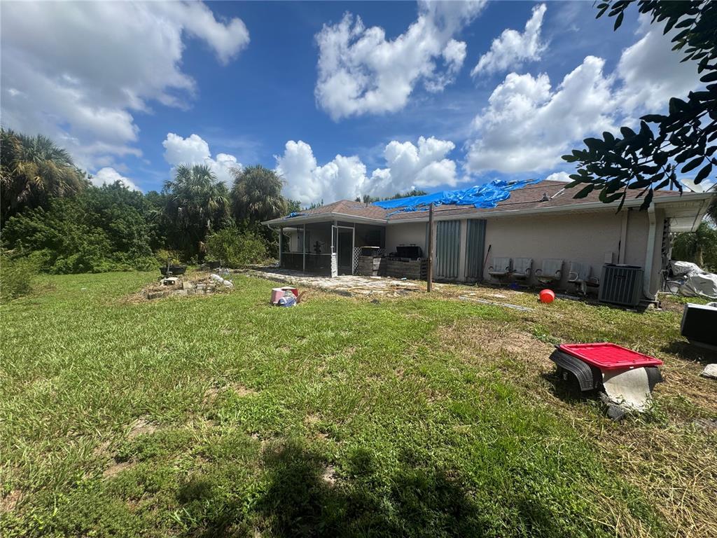 The backyard of a house features a patio, a blue tarp on the roof, and lawn — 168 MILLPORT STREET NW, PORT CHARLOTTE, FL