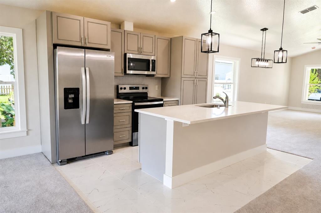 A kitchen with grey cabinets, stainless steel appliances, a white island, and light-colored tile flooring — 507 FINLEY AVENUE, KISSIMMEE, FL