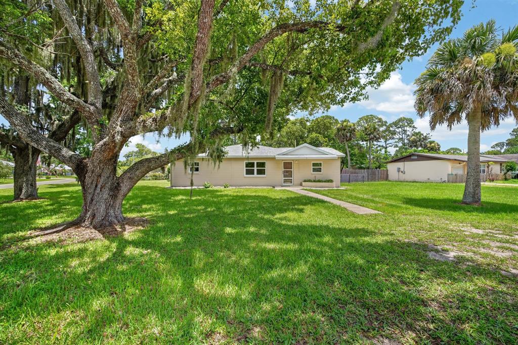 A single-story beige house sits on a grassy lot shaded by large, moss-covered oak trees — 2205 JUNIPER DRIVE, EDGEWATER, FL