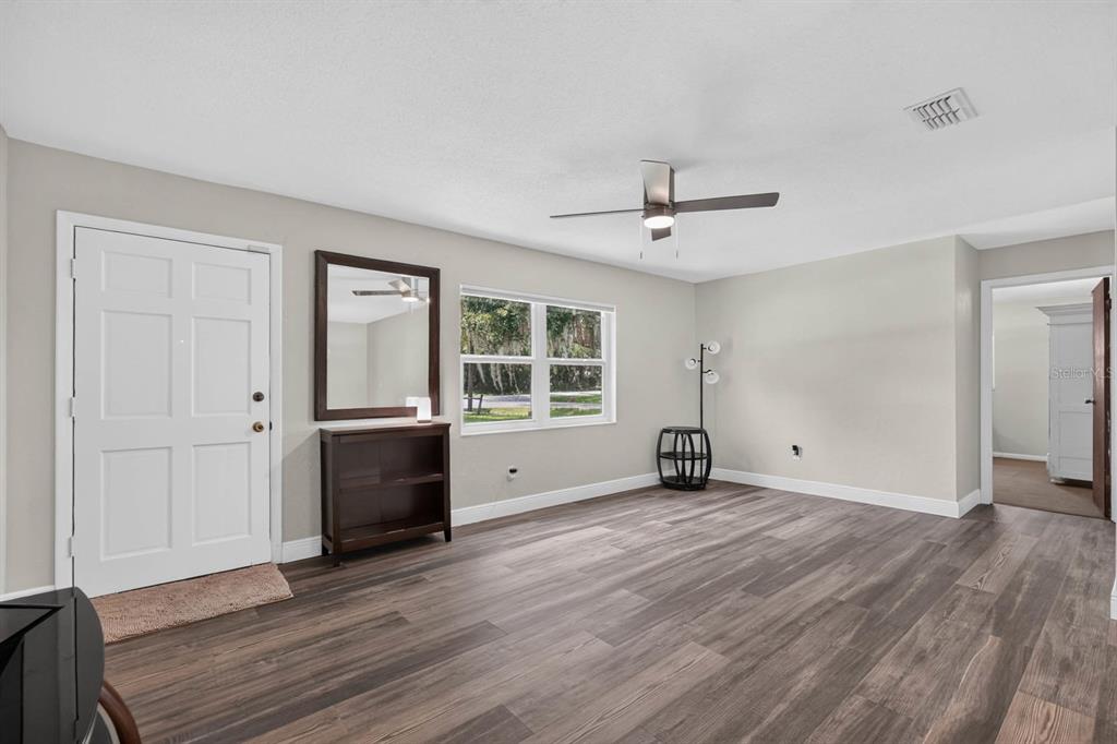 A living room with light gray walls, wood-look flooring, a ceiling fan, and a front door — 2205 JUNIPER DRIVE, EDGEWATER, FL