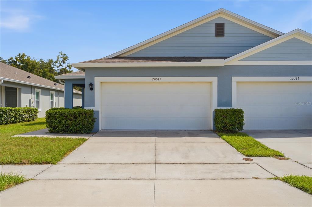 A blue and white duplex exterior features two garage doors and a concrete driveway — 20043 ROYAL TERN COURT, LEESBURG, FL
