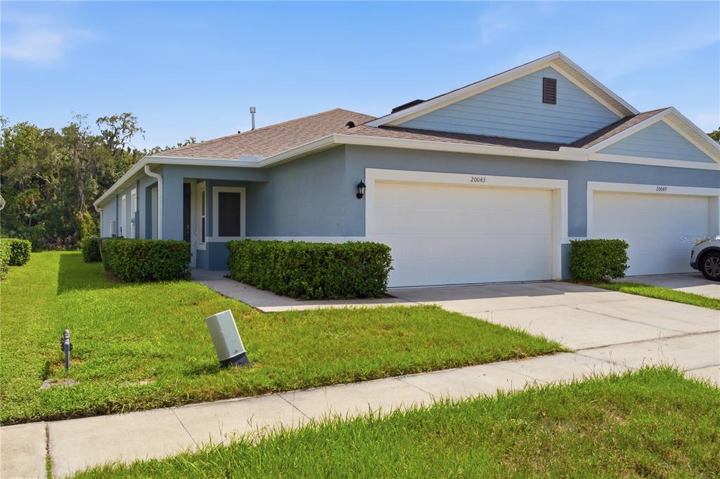 A blue, single-story duplex with a two-car garage and a landscaped front lawn — 20043 ROYAL TERN COURT, LEESBURG, FL