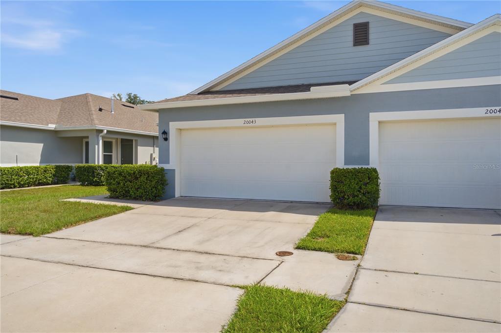 A view of a blue residential building with two garage doors and a concrete driveway — 20043 ROYAL TERN COURT, LEESBURG, FL