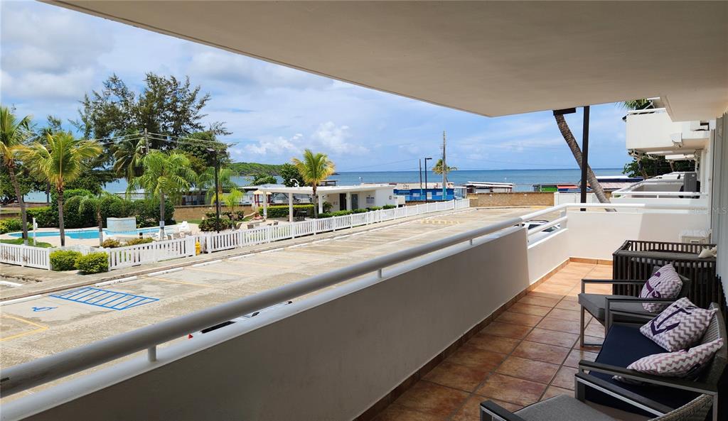 A balcony with tiled flooring and outdoor seating overlooks a parking lot and the ocean — C-201 PALMA VISTA COND, FAJARDO, PR