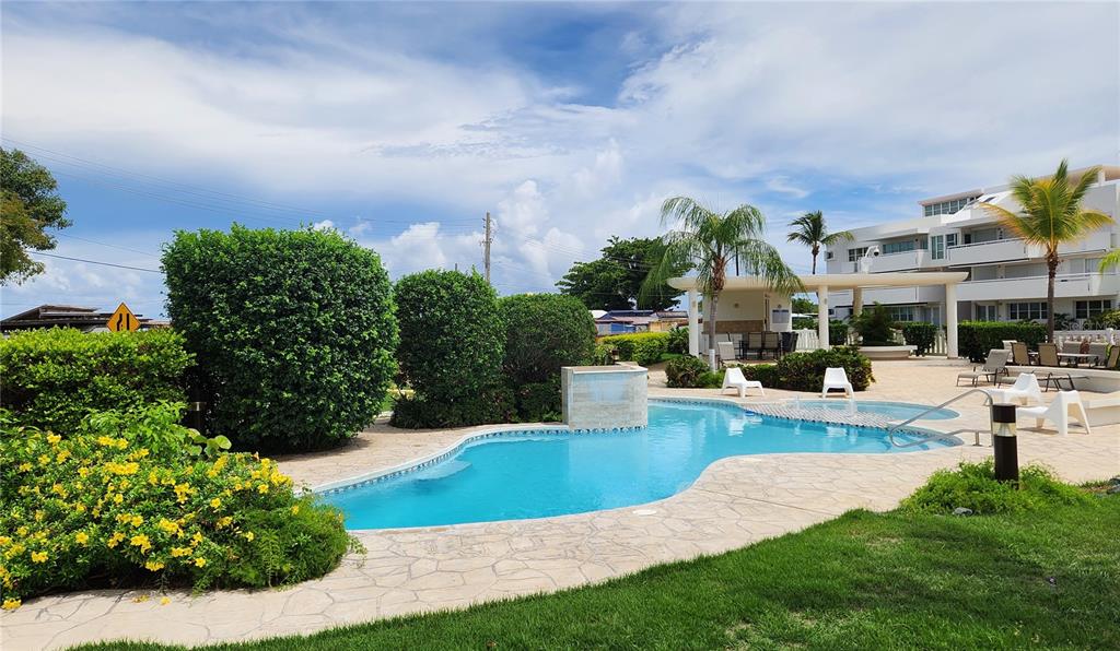 A swimming pool with a stone deck is surrounded by lush landscaping and a building — C-201 PALMA VISTA COND, FAJARDO, PR