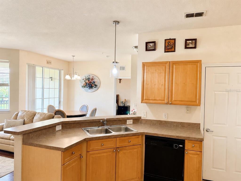 A kitchen with wood cabinets, laminate countertops, and a black dishwasher overlooks a dining area — 612 TERRACE RIDGE CIRCLE UNIT 126, DAVENPORT, FL