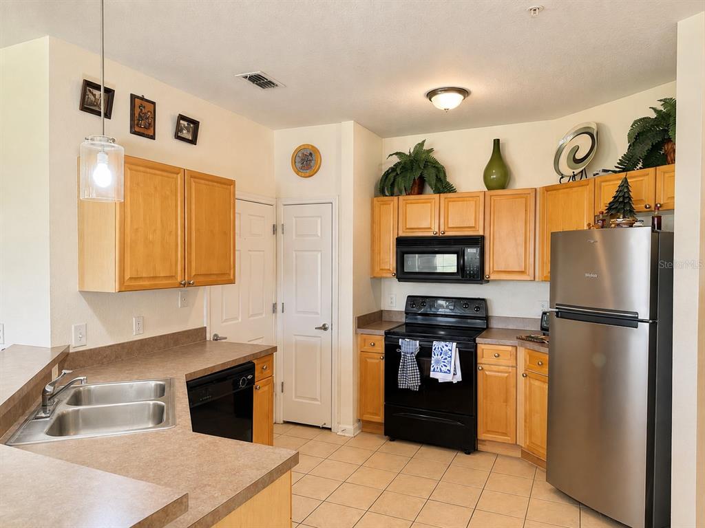 A kitchen features light wood cabinets, black appliances, a stainless steel sink, and tile flooring — 612 TERRACE RIDGE CIRCLE UNIT 126, DAVENPORT, FL
