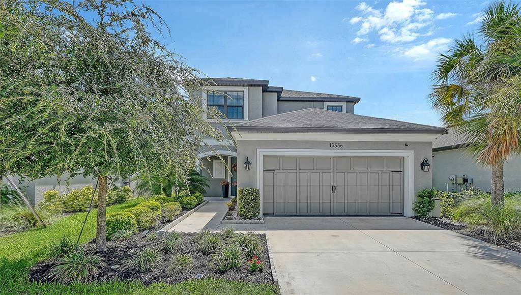 A two-story gray house features a two-car garage, a concrete driveway, and landscaped front yard — 15336 ISLA PALMA LANE, NOKOMIS, FL