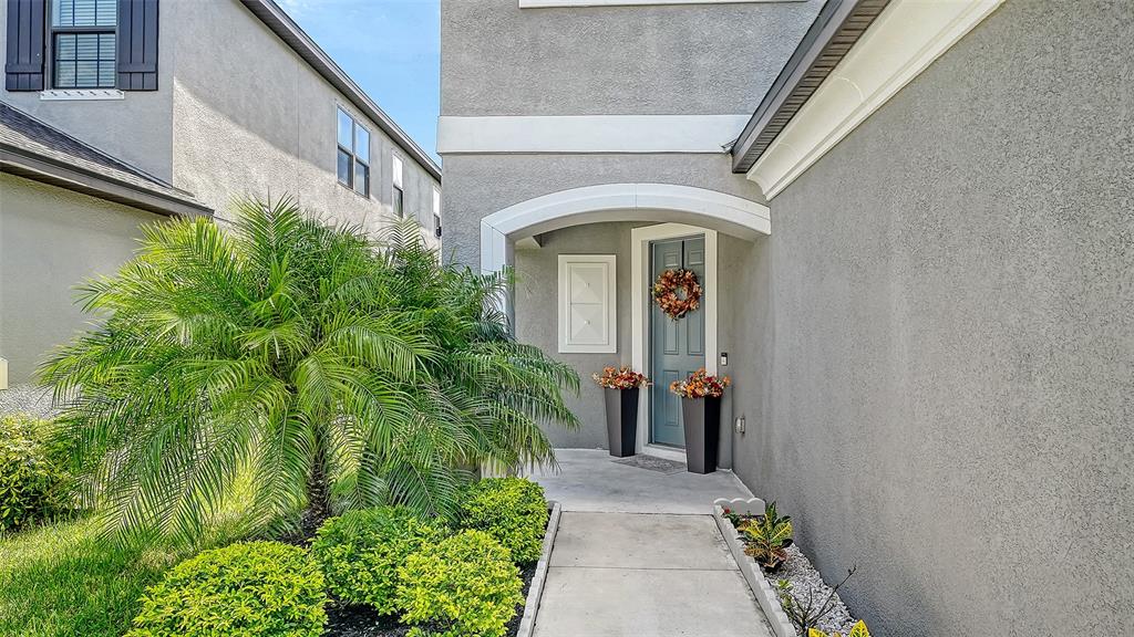A gray stucco house exterior features a front door with a wreath and potted plants — 15336 ISLA PALMA LANE, NOKOMIS, FL