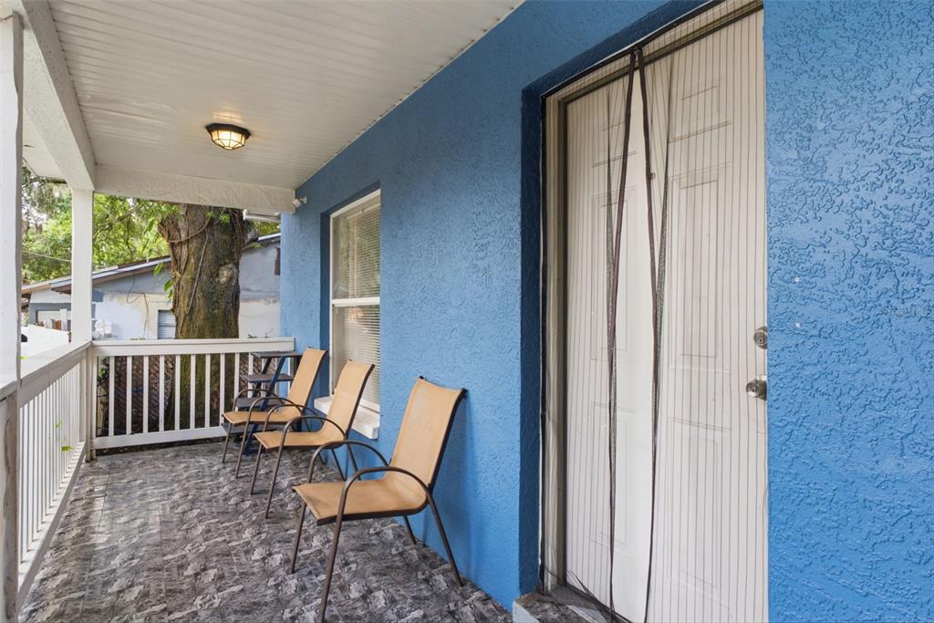 A covered porch with blue stucco walls, tiled flooring, and three tan chairs — 3203 DELEUIL AVENUE, TAMPA, FL