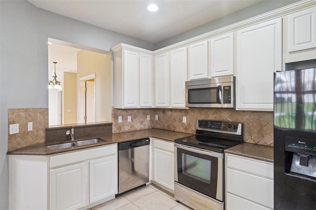 A kitchen with white cabinets, stainless steel appliances, brown countertops, and a tiled backsplash — 722 CHACALL LOOP, MOUNT DORA, FL