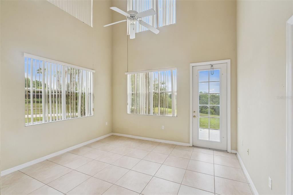A bright, tiled sunroom features a high ceiling, a ceiling fan, and a glass-paneled door — 722 CHACALL LOOP, MOUNT DORA, FL