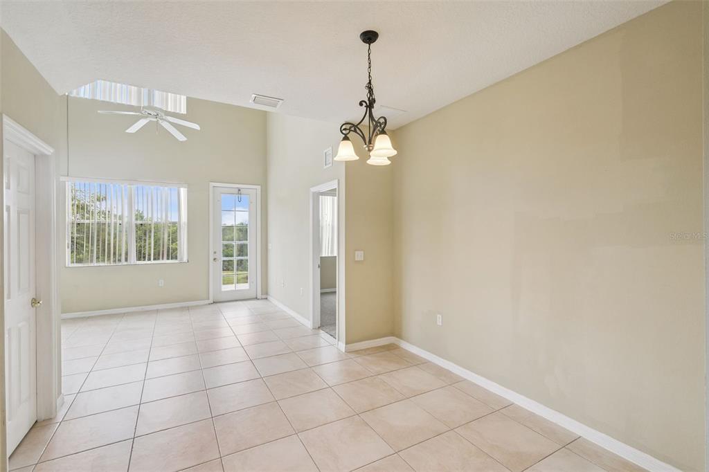 A bright room with beige tile floors, a vaulted ceiling, and a dining area chandelier — 722 CHACALL LOOP, MOUNT DORA, FL