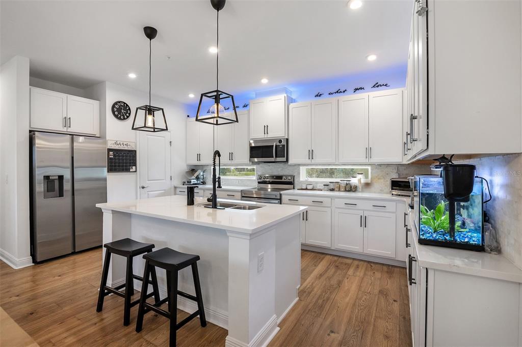 A modern open-concept kitchen with a white island, stainless steel appliances, and wood flooring — 7251 NEMOURS PARKWAY, ORLANDO, FL