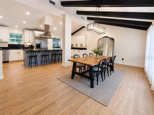 An open-concept kitchen and dining area features white cabinetry, wood flooring, and exposed ceiling beams — 1909 OLD SAWMILL ROAD, BRANDON, FL