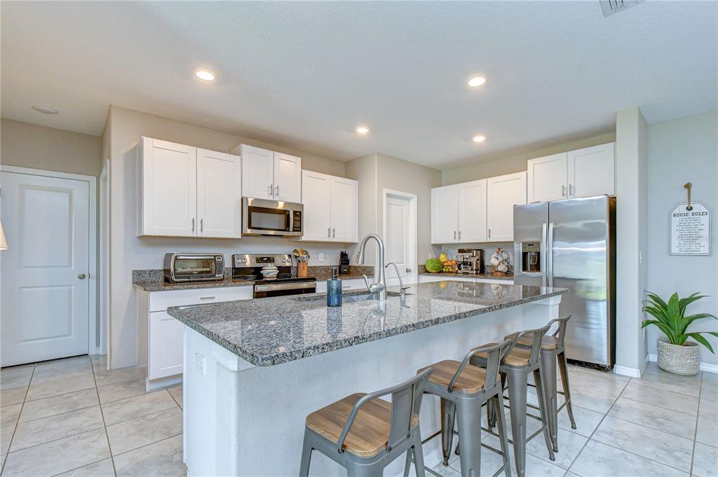 A kitchen features white cabinets, granite countertops, a central island with bar stools, and appliances — 17917 CLOUDLESS BLISS DRIVE, LUTZ, FL