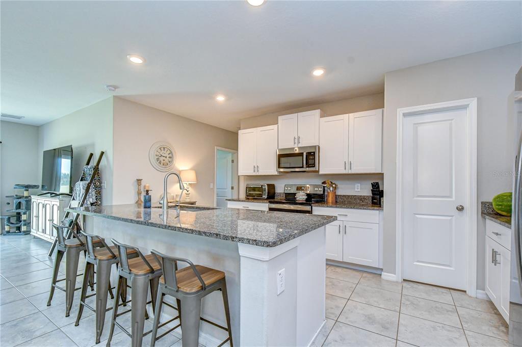 A kitchen features a granite-topped island with bar stools, white cabinetry, and tile flooring — 17917 CLOUDLESS BLISS DRIVE, LUTZ, FL