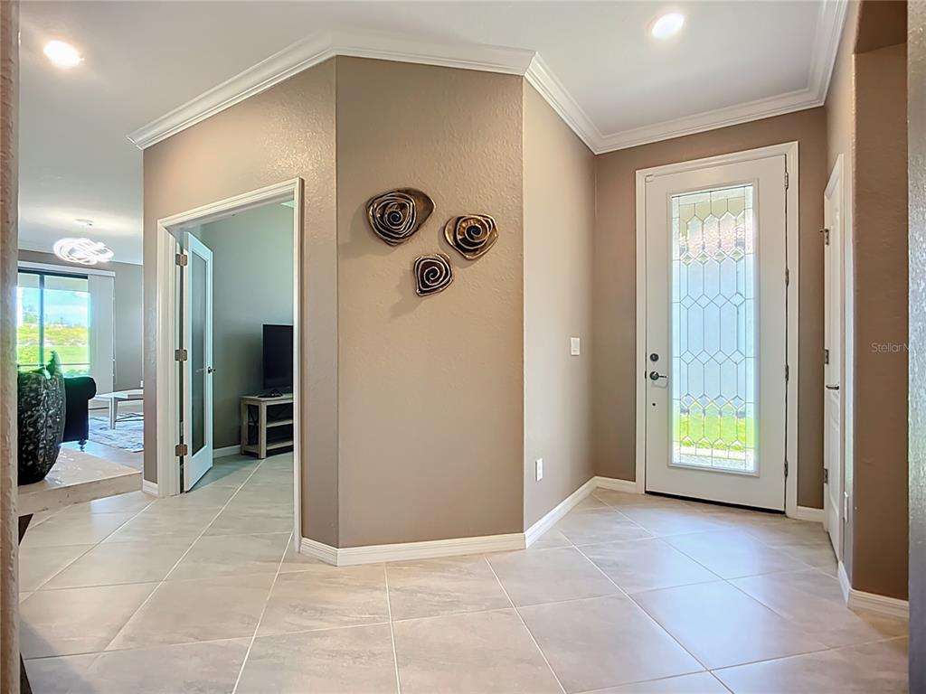 An entryway with tile flooring, a glass-paneled front door, and wall-mounted spiral art pieces — 24137 SPARTINA DRIVE, VENICE, FL