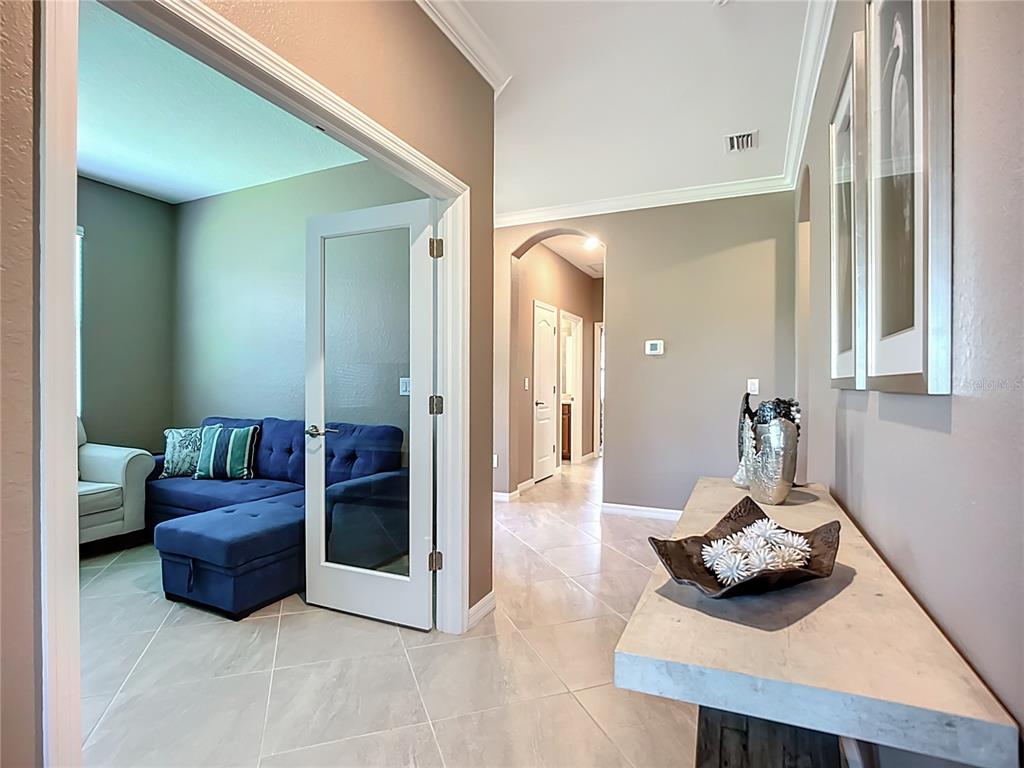 A hallway with tile flooring leads to a room with a blue sectional sofa — 24137 SPARTINA DRIVE, VENICE, FL