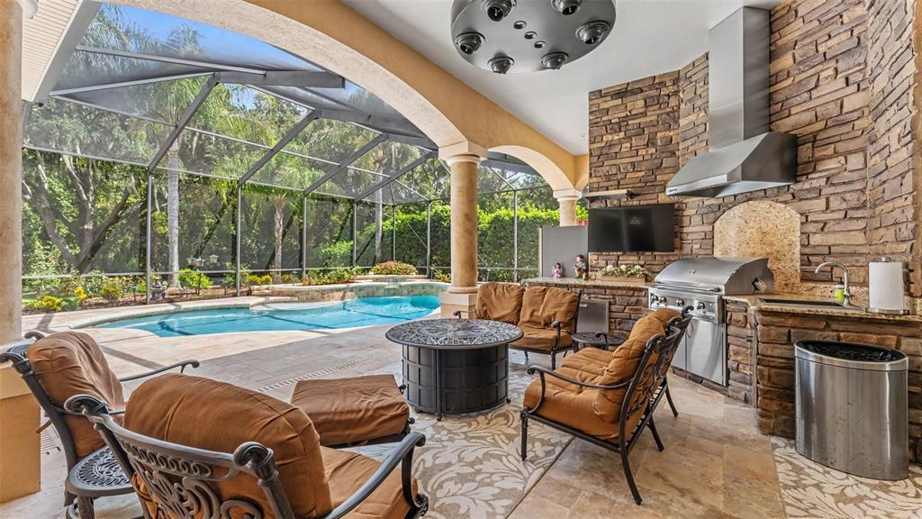 A covered outdoor patio features a stone kitchen, fire pit, seating area, and swimming pool — 2943 OAK TREE LANE, LAKELAND, FL