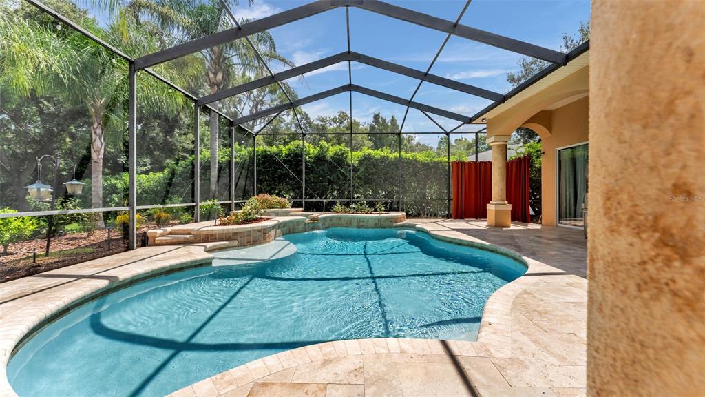A screened-in swimming pool with a raised spa and stone patio under a lanai — 2943 OAK TREE LANE, LAKELAND, FL