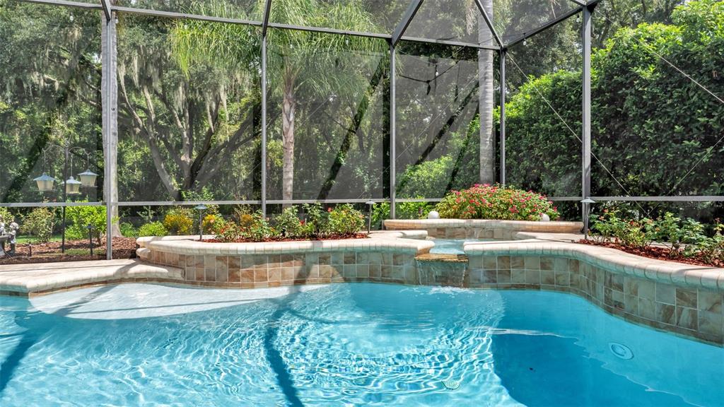A swimming pool with a raised stone spa and waterfall inside a screened-in pool enclosure — 2943 OAK TREE LANE, LAKELAND, FL
