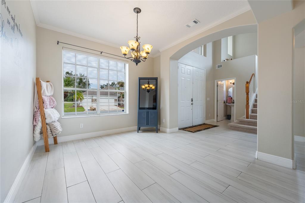 A bright dining area features light wood-look tile flooring, a chandelier, and a large window — 1524 THE OAKS BOULEVARD, KISSIMMEE, FL