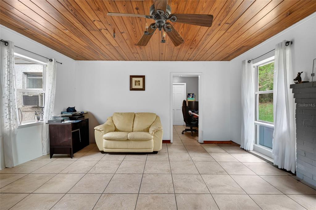 A living room features a wood-paneled ceiling, tile flooring, a beige sofa, and two windows — 8023 STONE ROAD, APOPKA, FL