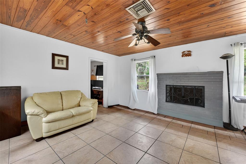 A living room with a wood-paneled ceiling, tiled floor, cream sofa, and gray brick fireplace — 8023 STONE ROAD, APOPKA, FL