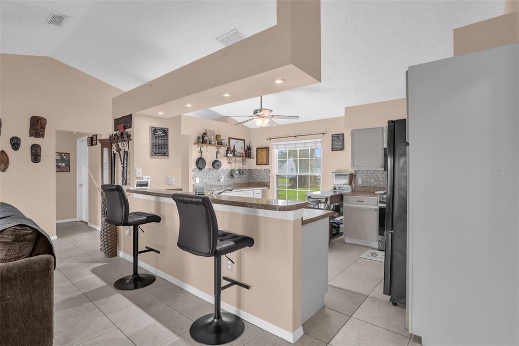 A kitchen with a breakfast bar, two stools, light cabinetry, and tiled flooring — 418 GROVEPARK DRIVE, DAVENPORT, FL