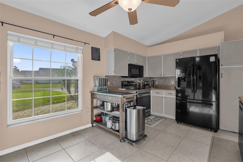 A kitchen features light-colored cabinets, black appliances, a rolling kitchen island, and tile flooring — 418 GROVEPARK DRIVE, DAVENPORT, FL