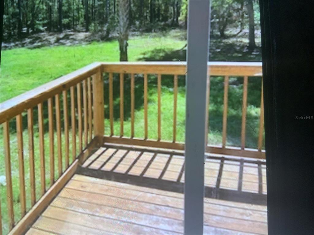 A wooden deck with railings overlooks a grassy yard and trees viewed through a window — 13080 NW 168TH PLACE, REDDICK, FL