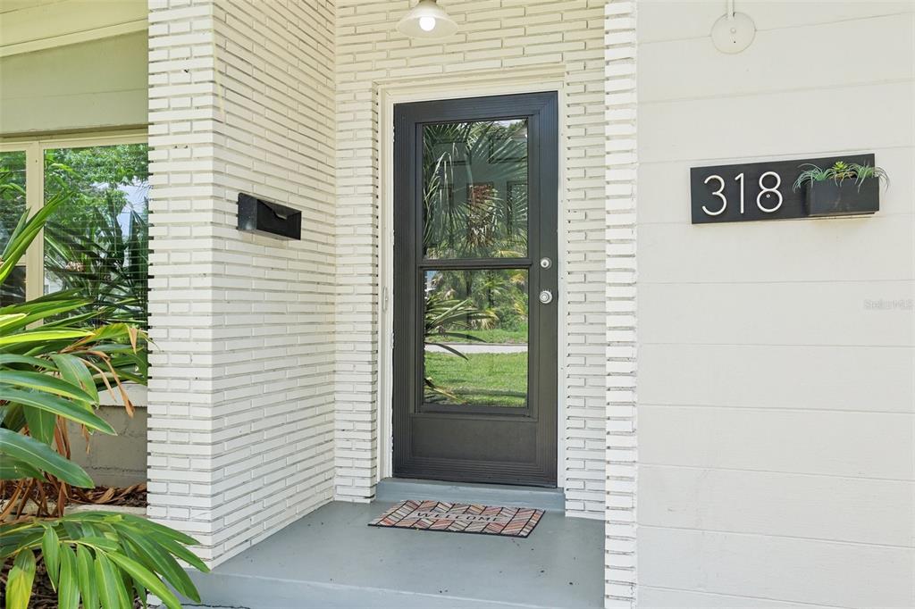 A front entryway features a black storm door, white brick siding, and a house number sign — 318 E JERSEY STREET, ORLANDO, FL