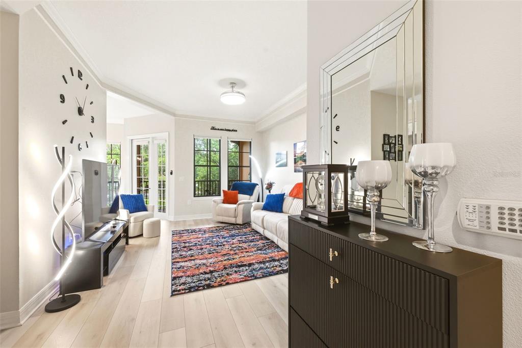A living room features light wood flooring, a colorful area rug, and a wall-mounted clock — 500 MIRASOL CIRCLE UNIT 205, CELEBRATION, FL
