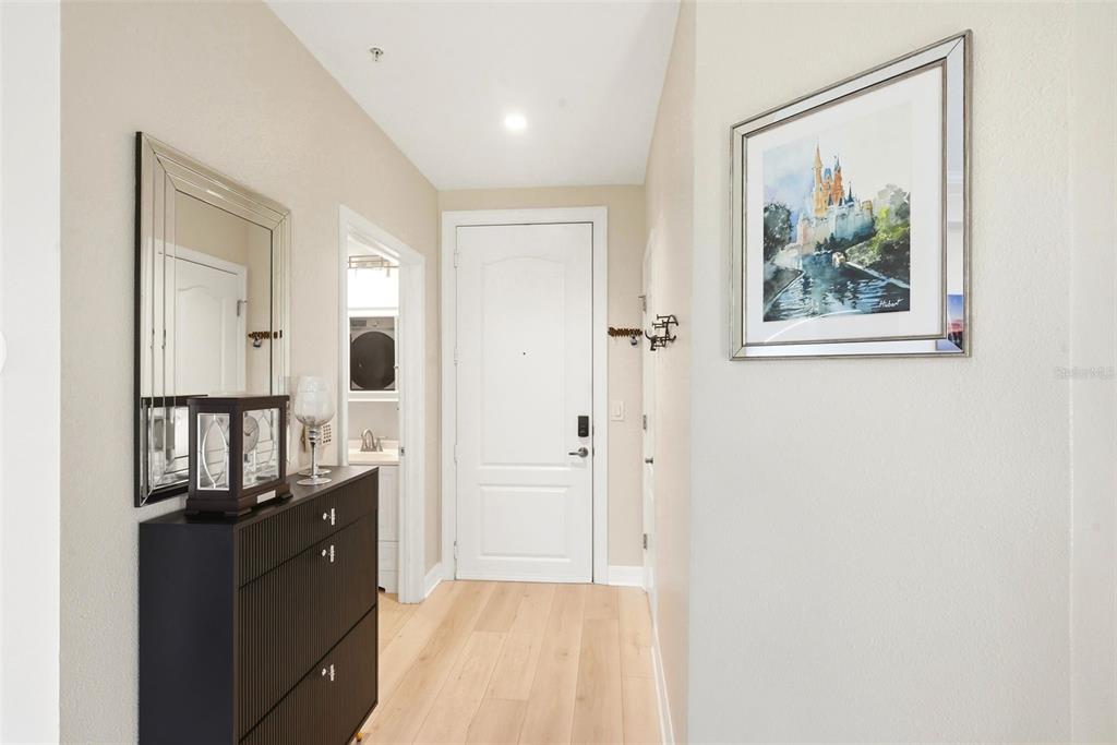 A hallway features light wood flooring, a black storage cabinet, a mirror, and a framed print — 500 MIRASOL CIRCLE UNIT 205, CELEBRATION, FL