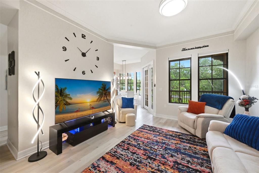 A living room features a large wall clock, a television on a stand, and seating — 500 MIRASOL CIRCLE UNIT 205, CELEBRATION, FL